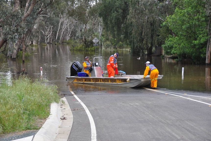 SES volunteers push a boat onto a flooded road.