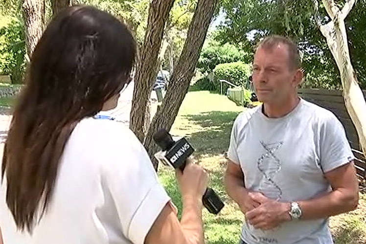 A woman with a microphone speaks with a man in shorts and a t-shirt