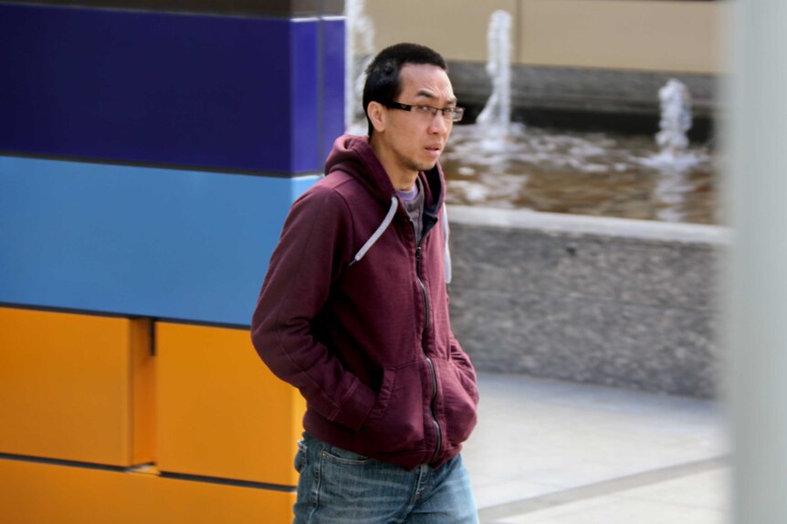 Josh Nguyen, black hair and glasses, walks with hands in maroon hoodie, exiting Federal Court building.