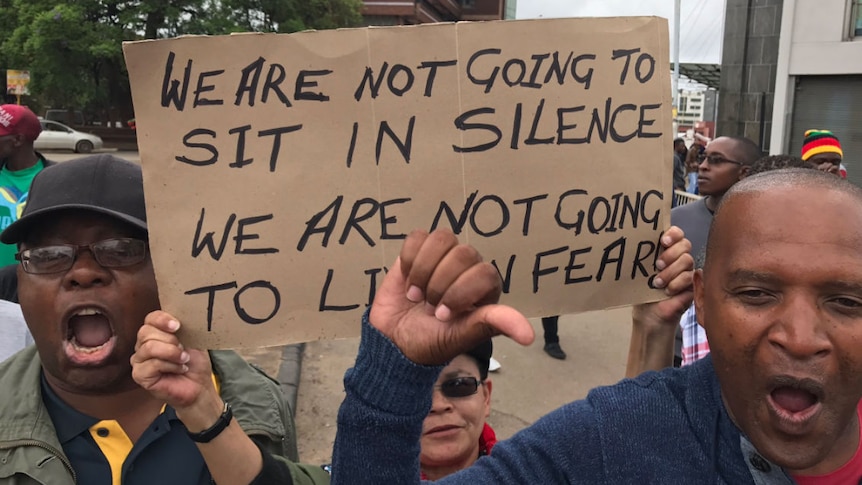 People hold a sign which reads the lyrics to John Farnham's song, The Voice: "we're not going to sit in silence"