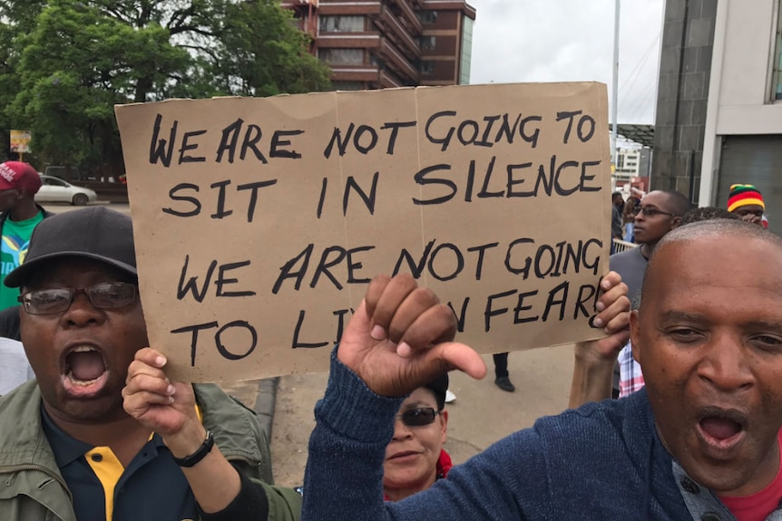 People hold a sign which reads the lyrics to John Farnham's song, The Voice: "we're not going to sit in silence"