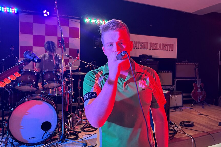 Teenage boy wearing green shirt singing at a microphone. 
