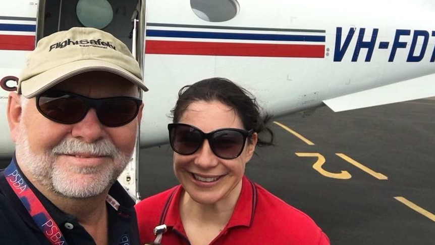 Husband and wife standing in front of plane on the tarmac.