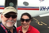 Husband and wife standing in front of plane on the tarmac.