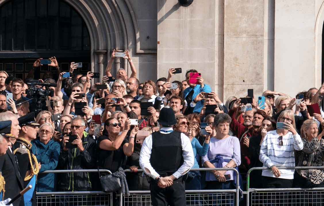 Vista ingrandita della folla, con diverse persone che fotografano la processione