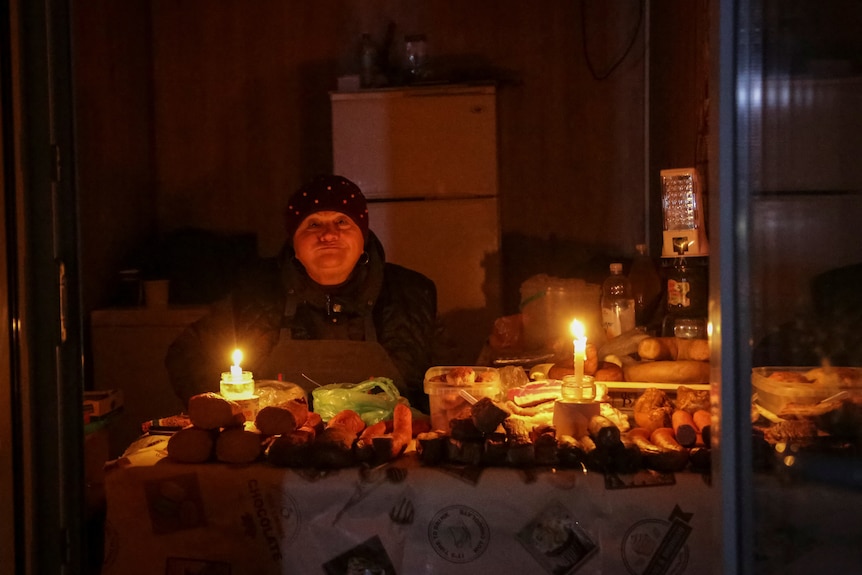 A vendor waits for customers in a small store that is lit with candles.
