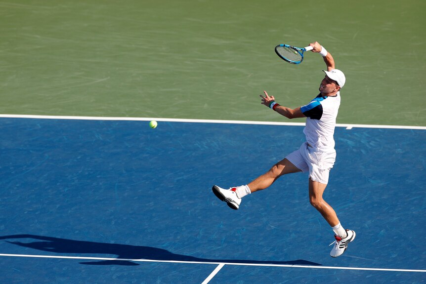 James Duckworth runs backwards and plays an overhead shot on the blue court at the US Open