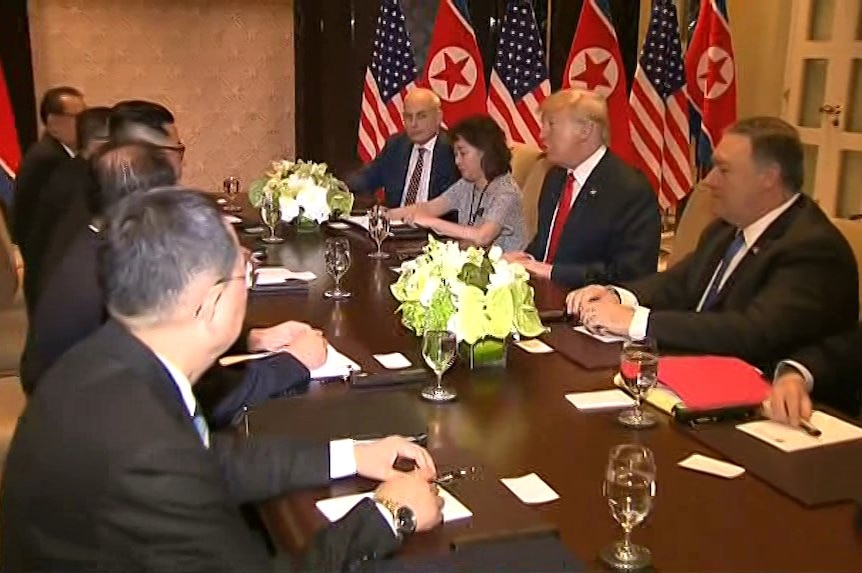Donald Trump and his advisers sit opposite Kim Jong-un and his advisers at a table.