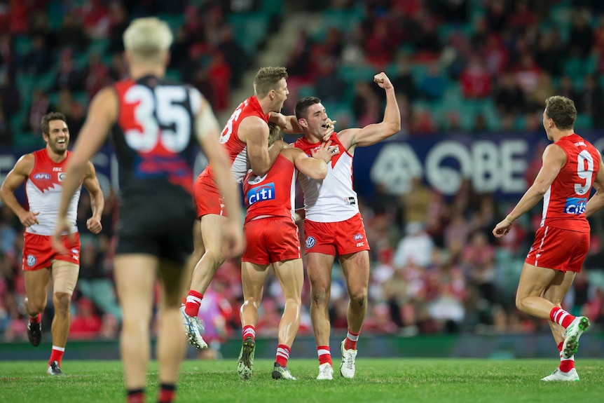 Teammates surround an AFL player who punches the air having kicked a goal.