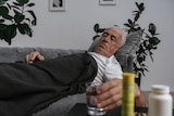Older man lies on couch and reaches for a glass of water.