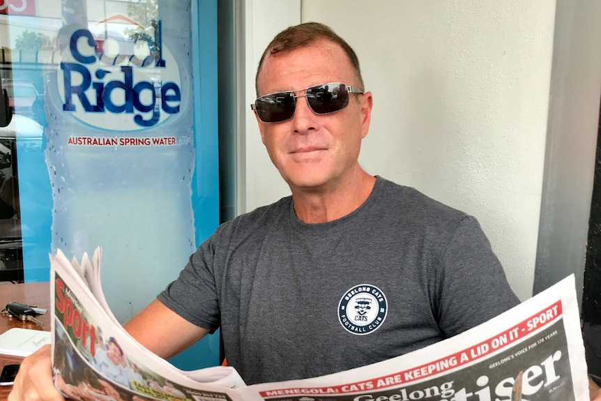 A man wearing sunglasses reading the Geelong Advertiser newspaper.