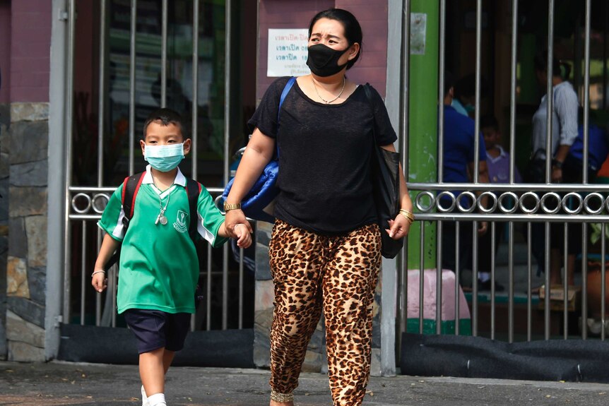 A mum picks up her child up from school, both are wearing protective masks due to the high levels of air pollution.