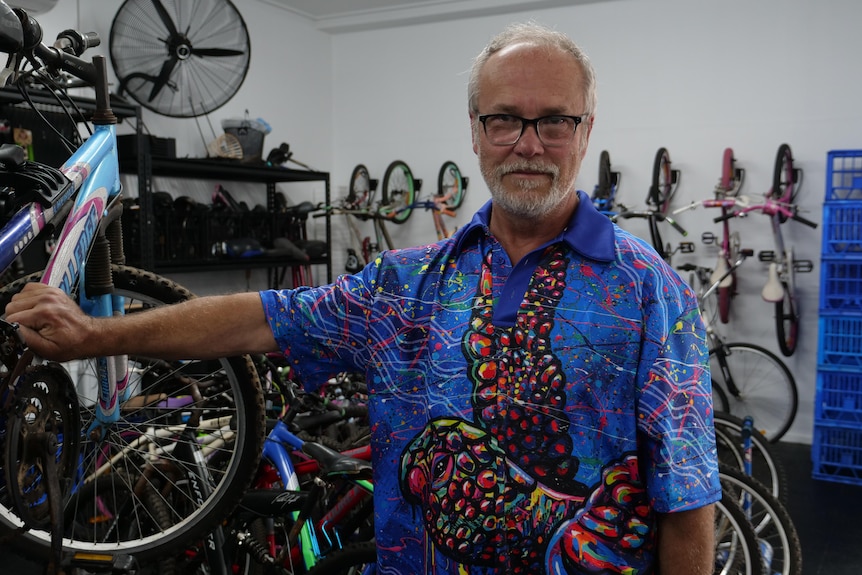 A man with grey hair and a beard stands in a room with bikes in the background