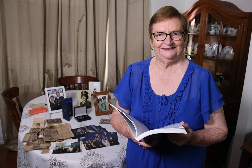 Ros Peters standing in front of her medals and old photographs during her time as a QPS officer.