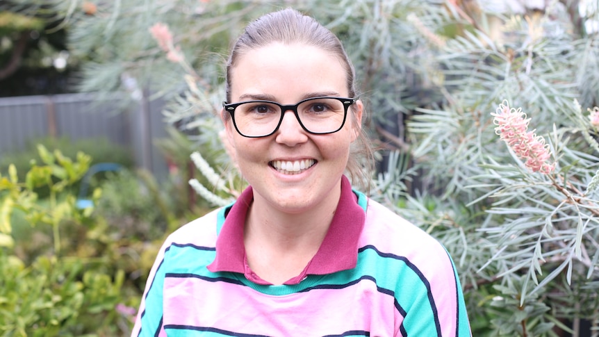 A woman wearing glasses stands in front of some flowers