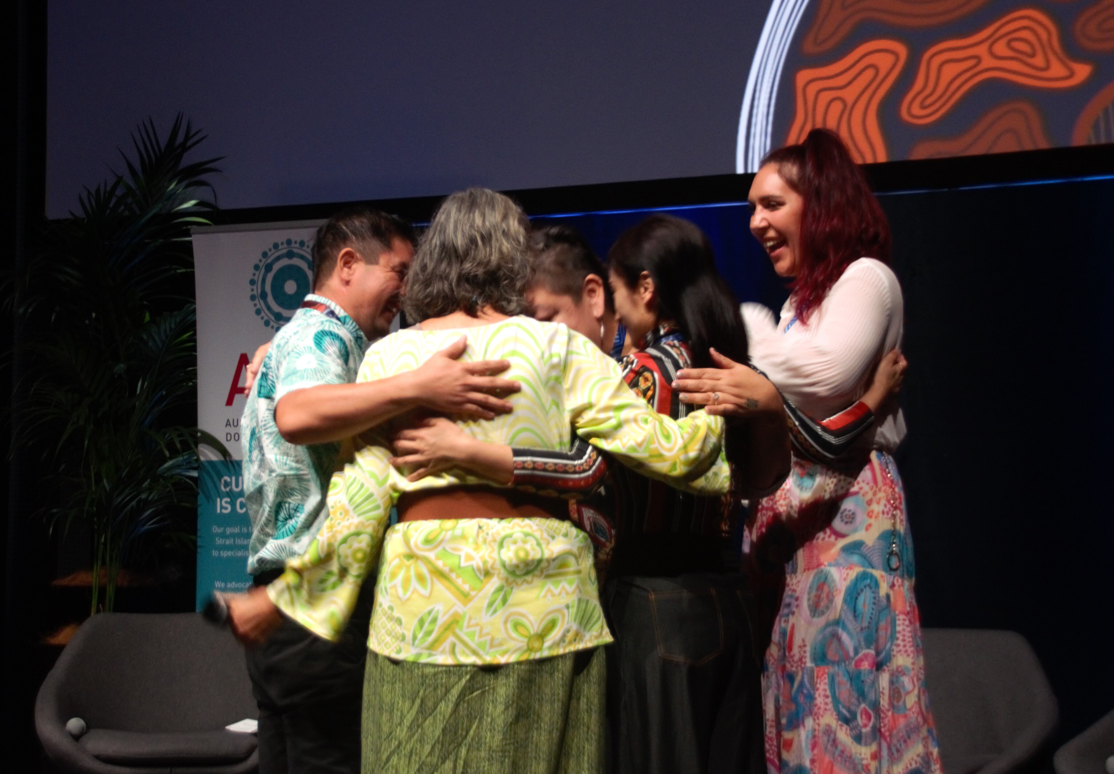 Five people hug on a stage