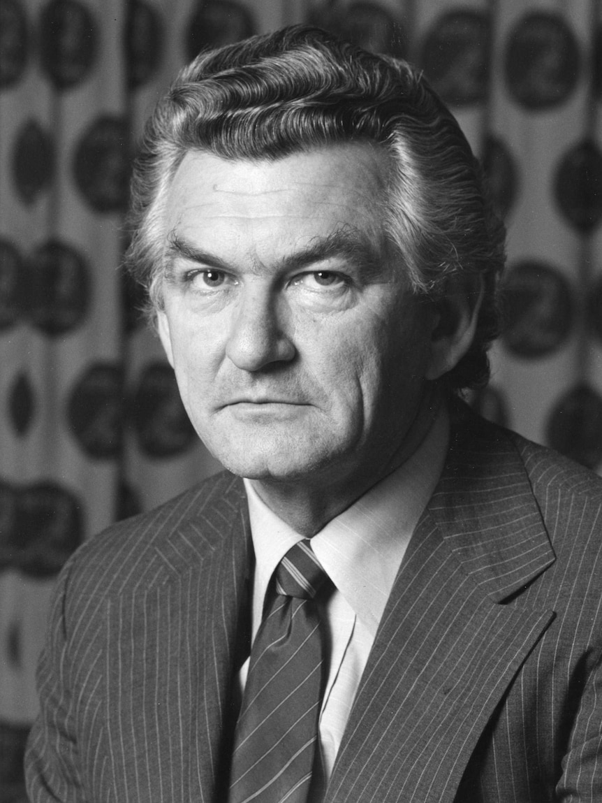 Bob Hawke, wearing pinstripe suit and tie, looks at the camera, patterned curtain in background.