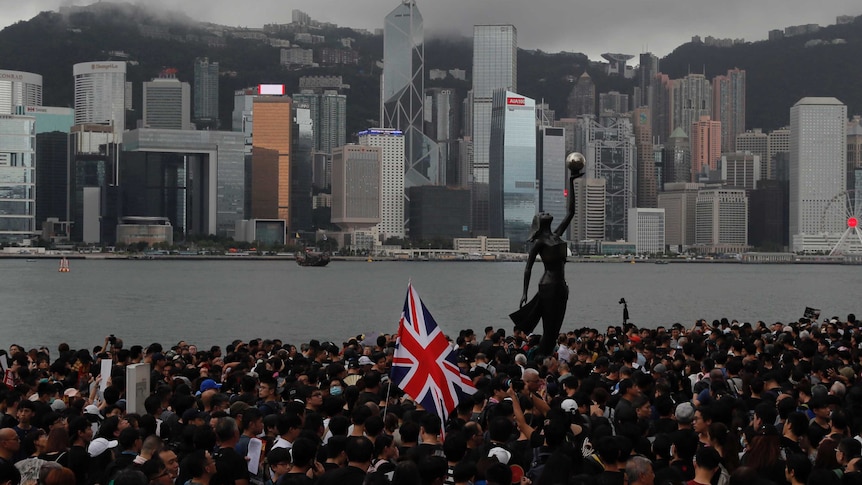 Thousands of Hong Kong protesters carry a British flag by the harbour.