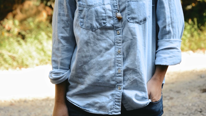 Close up of a woman wearing a chambray button-down shirt with a hand tucked into her jeans pocket.