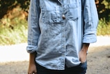 Close up of a woman wearing a chambray button-down shirt with a hand tucked into her jeans pocket.