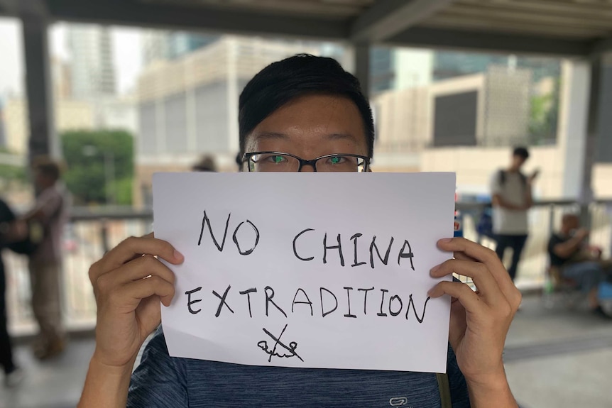 In a dark footbridge, a Hong Kong protestor covers two-thirds of his face behind a white A4 sheet.