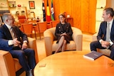 two men and a women in business suits share a joke around a coffee table in an office