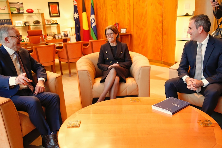 two men and a women in business suits share a joke around a coffee table in an office