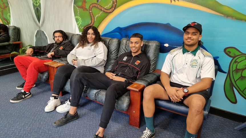 Four young people sitting in front of a mural in their classroom