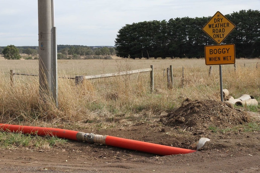 An orange pipe runs near a road sign that says "Dry Weather Road Only - Boggy When Wet".
