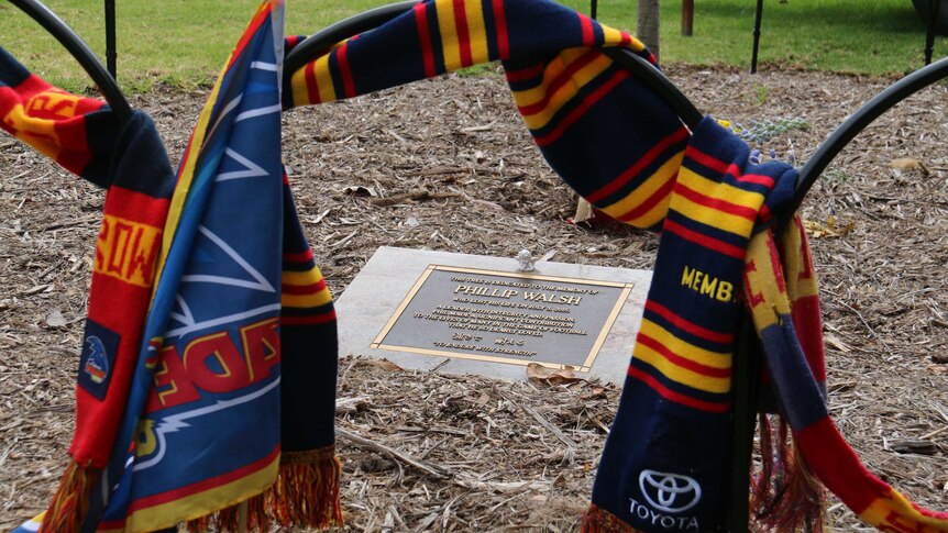 Two Crows scarfs hung around a memorial plaque to former Adelaide coach Phil Walsh