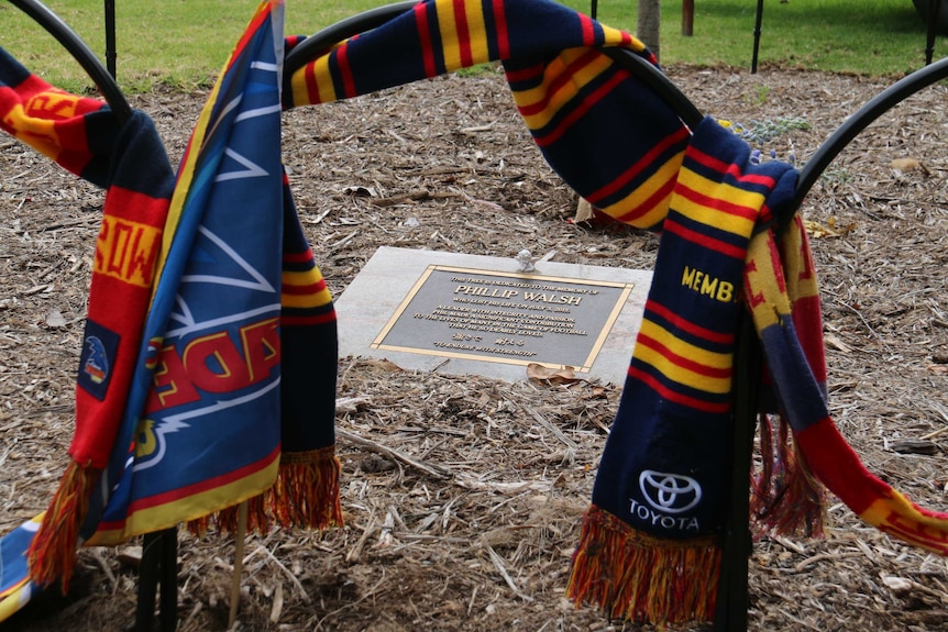 Two Crows scarfs hung around a memorial plaque to former Adelaide coach Phil Walsh