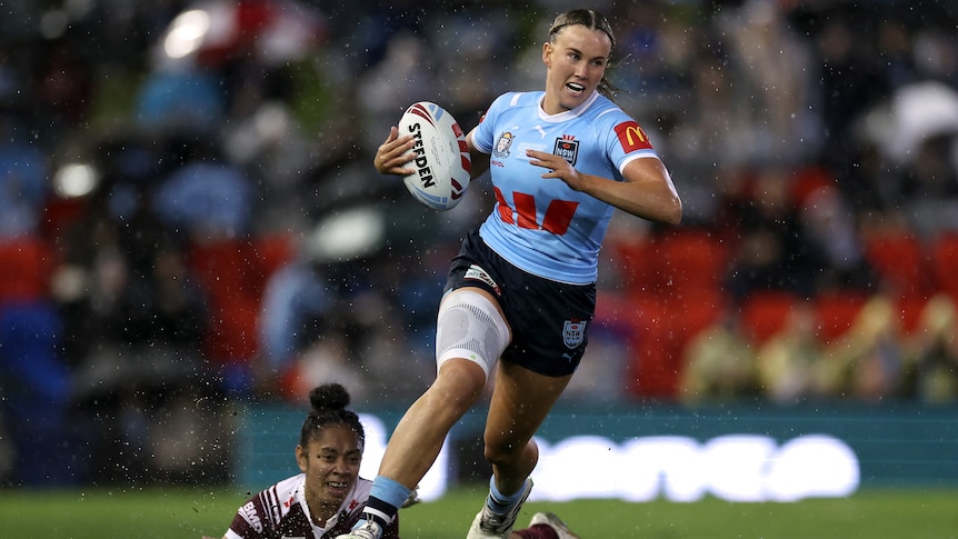 NSW Sky Blues player Jaime Chapman runs with the ball in Women's State of Origin as Queensland Maroons Emma Paki dives.