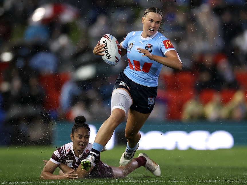 NSW Sky Blues player Jaime Chapman runs with the ball in Women's State of Origin as Queensland Maroons Emma Paki dives.