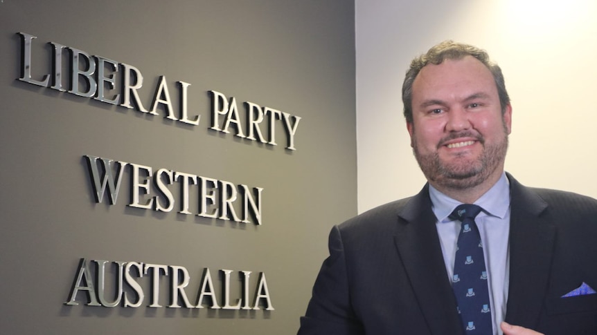 Richard Wilson in a suit and tie standing in front of signs that says "Liberal Party Western Australia" 