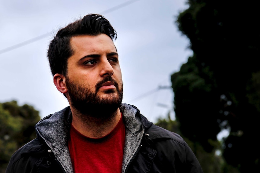 A man wearing a red shirt and black jacket looks thoughtfully towards the sky.