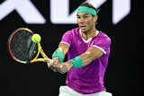 Brunette man in purple shirt, green bandana holds tennis racquet
