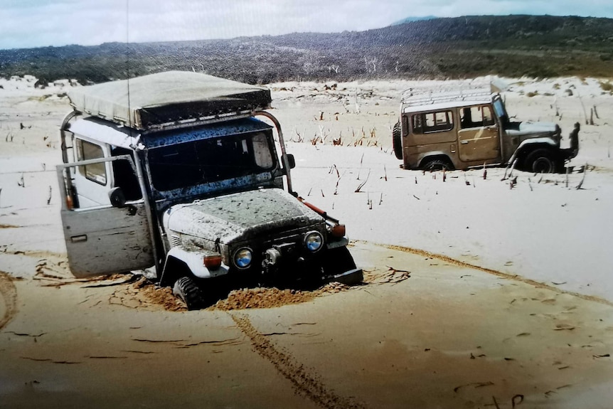 Two four wheel drives stuck deeply in sand with a sandy, scrubby background