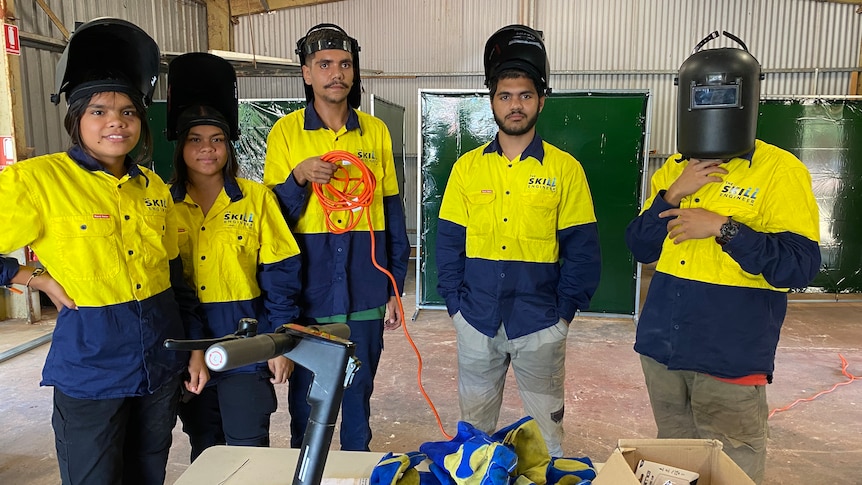 Five students wearing hi-vis tops and welding helmets
