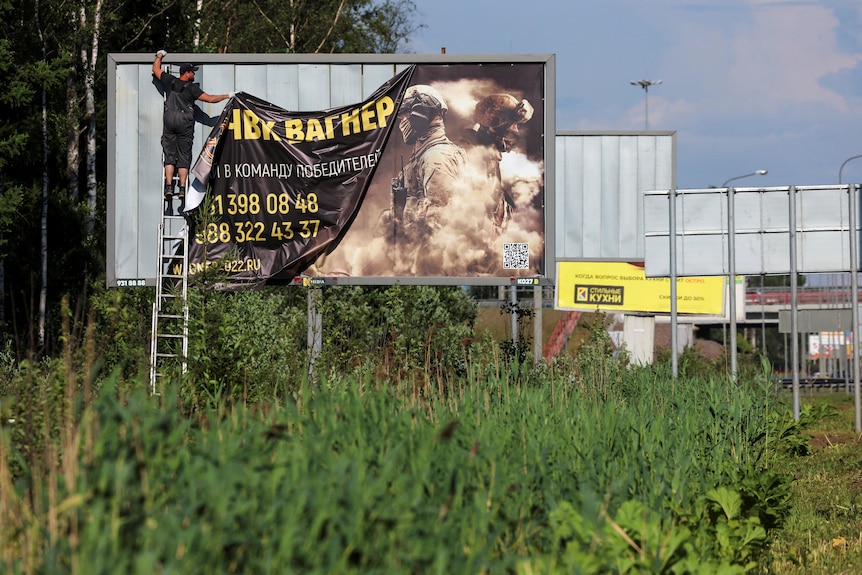 A worker removes a billboard ad promoting service in Wagner group in St Petersburg