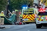 Ambulances next to a fallen motorbike, emergency services holding up a green sheet