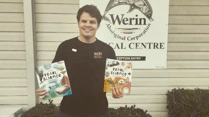 Young man holds DeadlyScience books and smiles to the camera