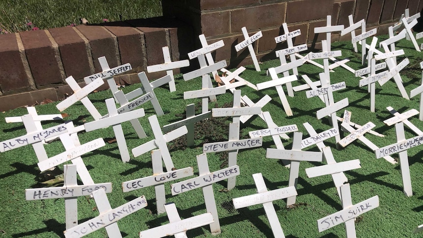 White crosses lie bent and damaged, wedged into green grass.