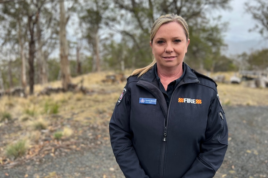 Sandra McCann stands in a bushy area and lwears a Tasmania Fire Service uniform