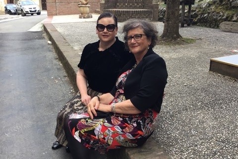 Two women dressed in black tops and colourful skirts sit on the side of the road