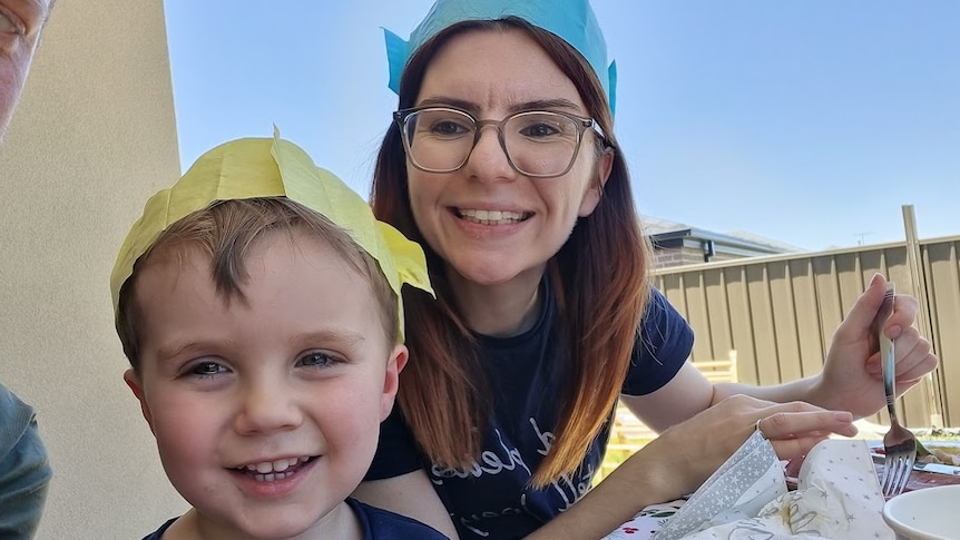 A boy and a woman, both wearing party hats, smile at the camera.