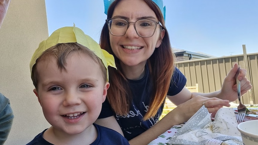 A boy and a woman, both wearing party hats, smile at the camera.