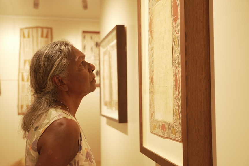 Woman stands close to framed artwork and stares at it