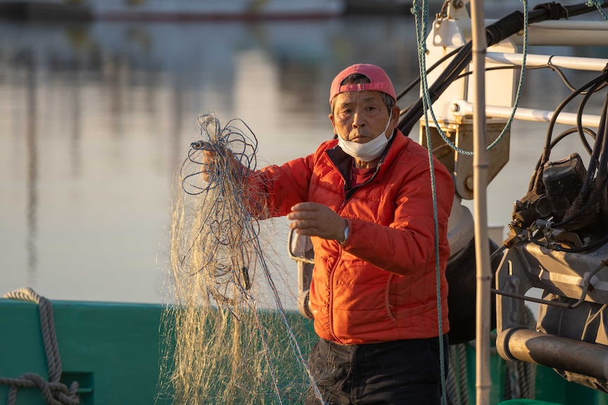 A man in a red puffy coat holding a bunch of fishing nets and rope on a boat