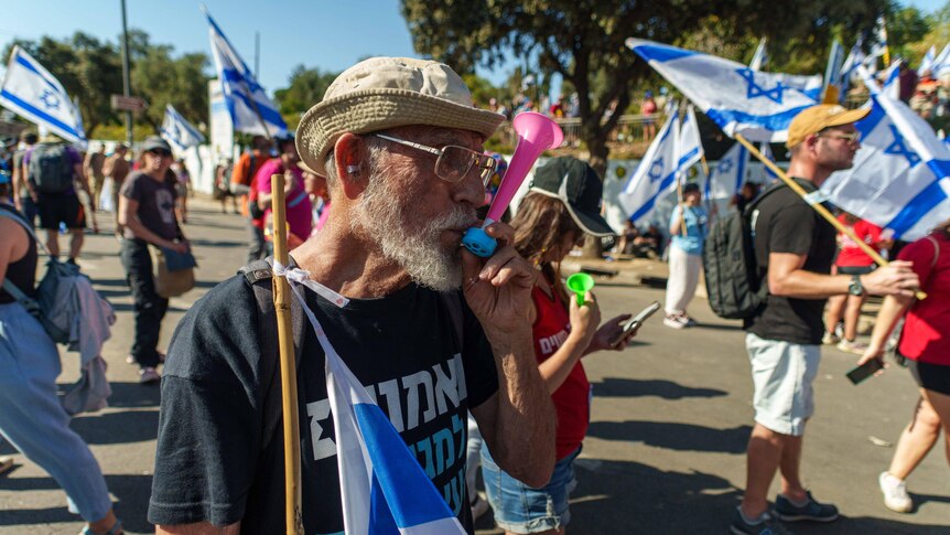 A man with a beard blows a whistle at a protest 