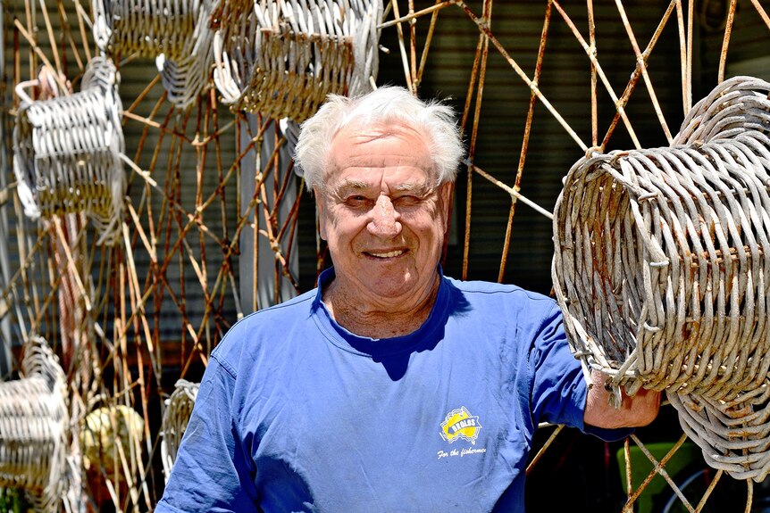 An old man leans against a wire fence decorated with cray pots